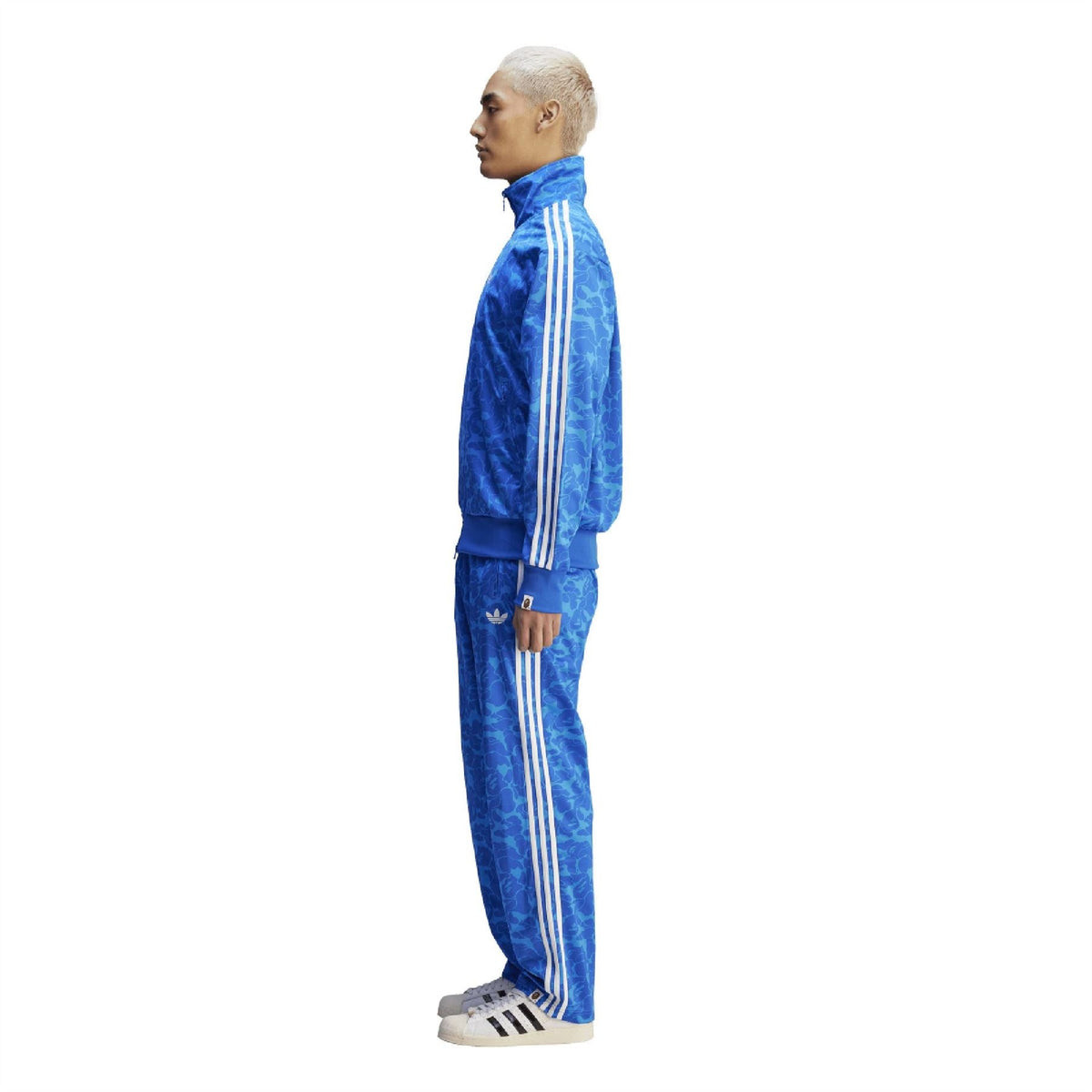 Blue camouflage track pants with white triple stripes, slim taper and cuffed ankle