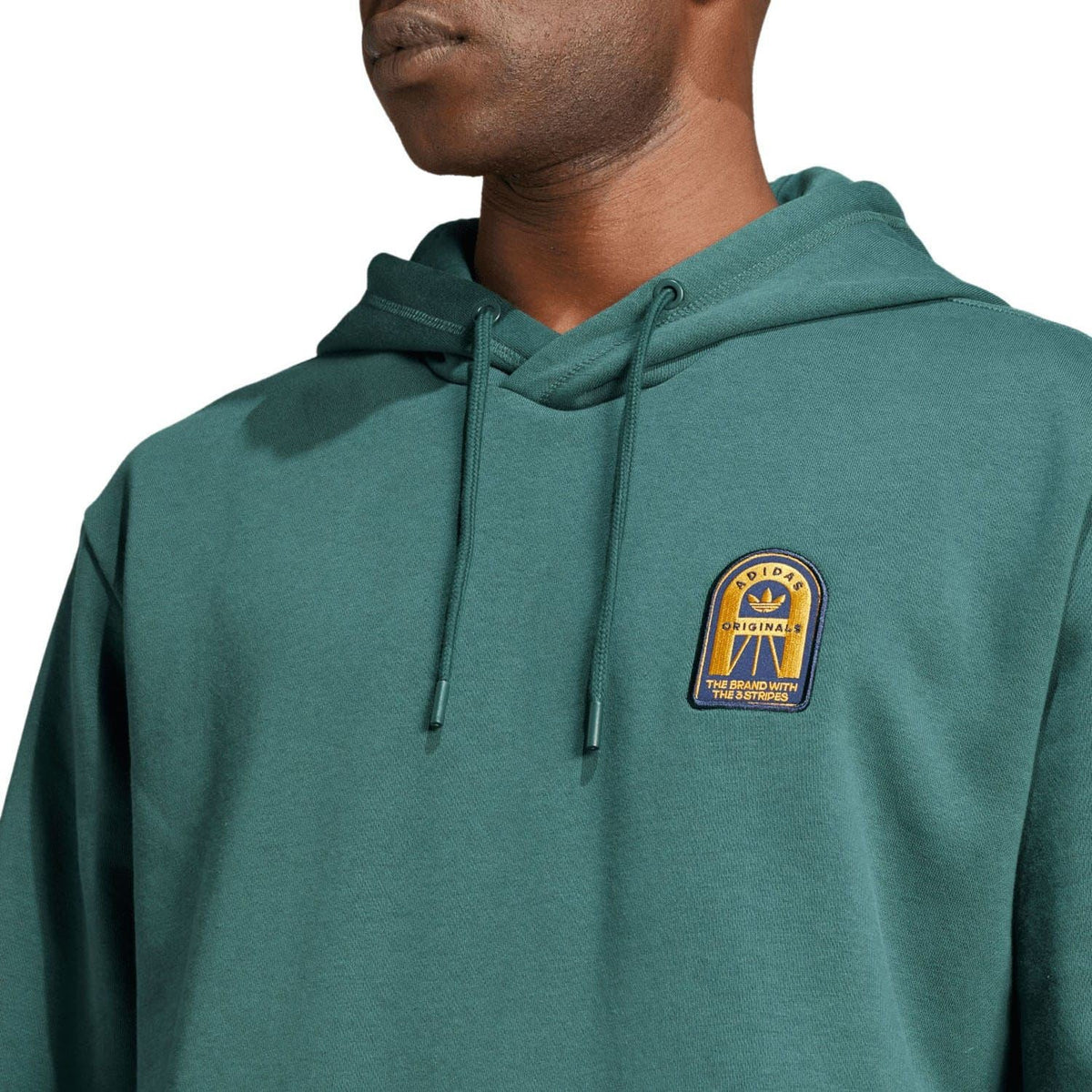 Green adidas Originals hoodie close-up of embroidered chest logo patch and drawstring hood