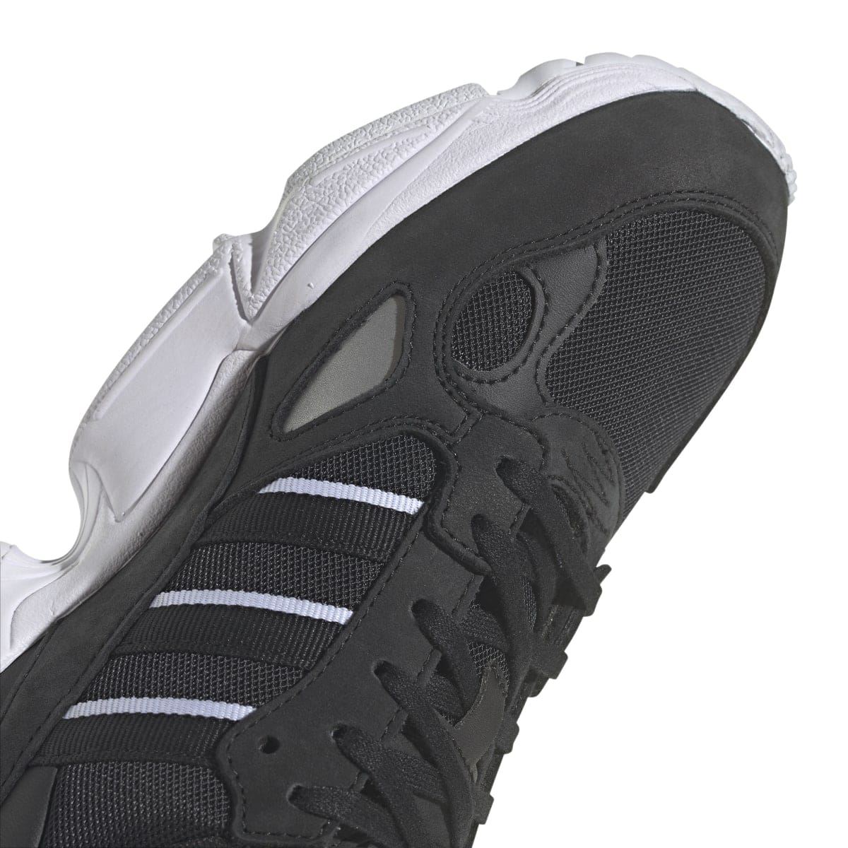 Close-up of black upper and lace area with white branding and three-stripe panel
