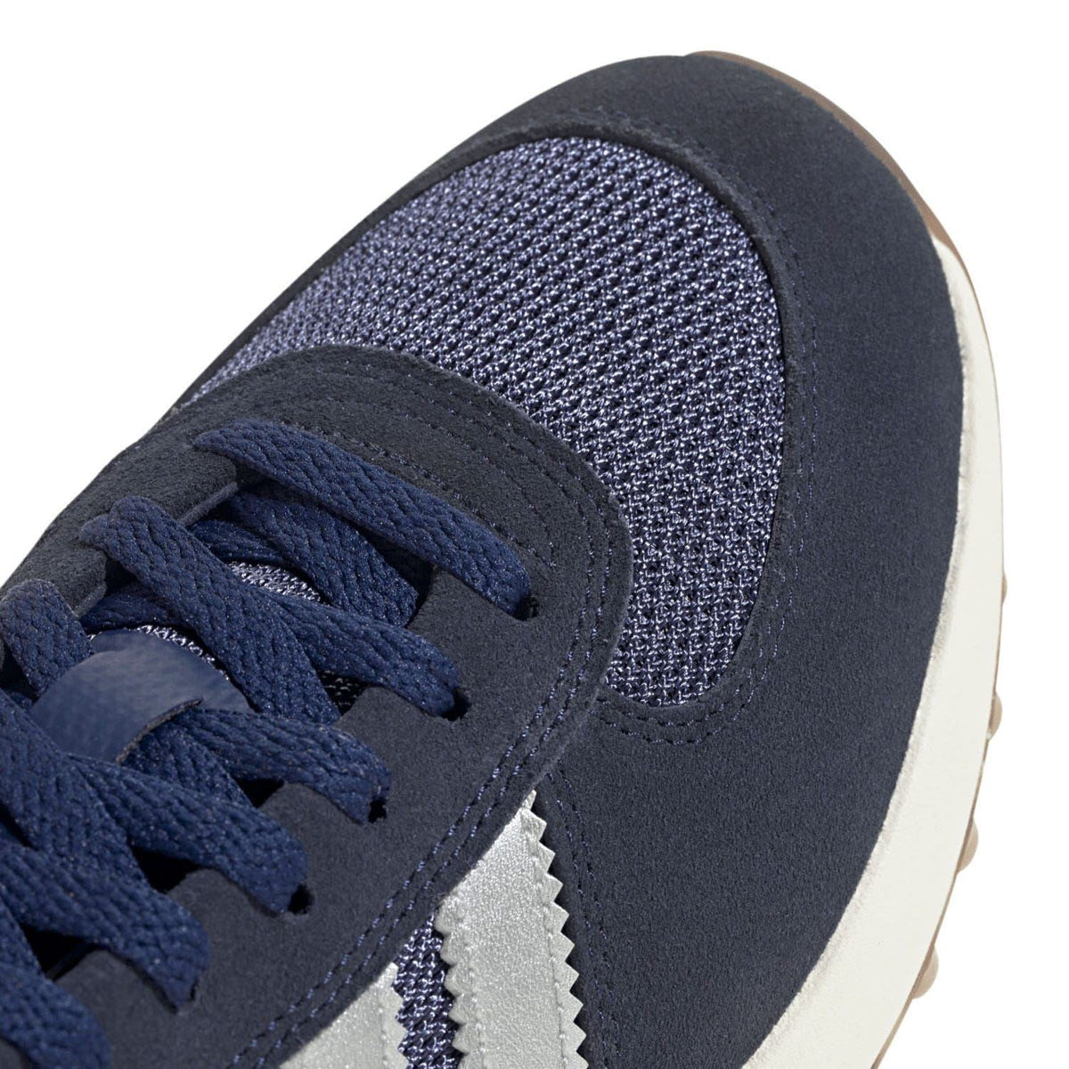 Navy sneaker upper close-up with textured fabric, suede panel, and lace-up eyelets