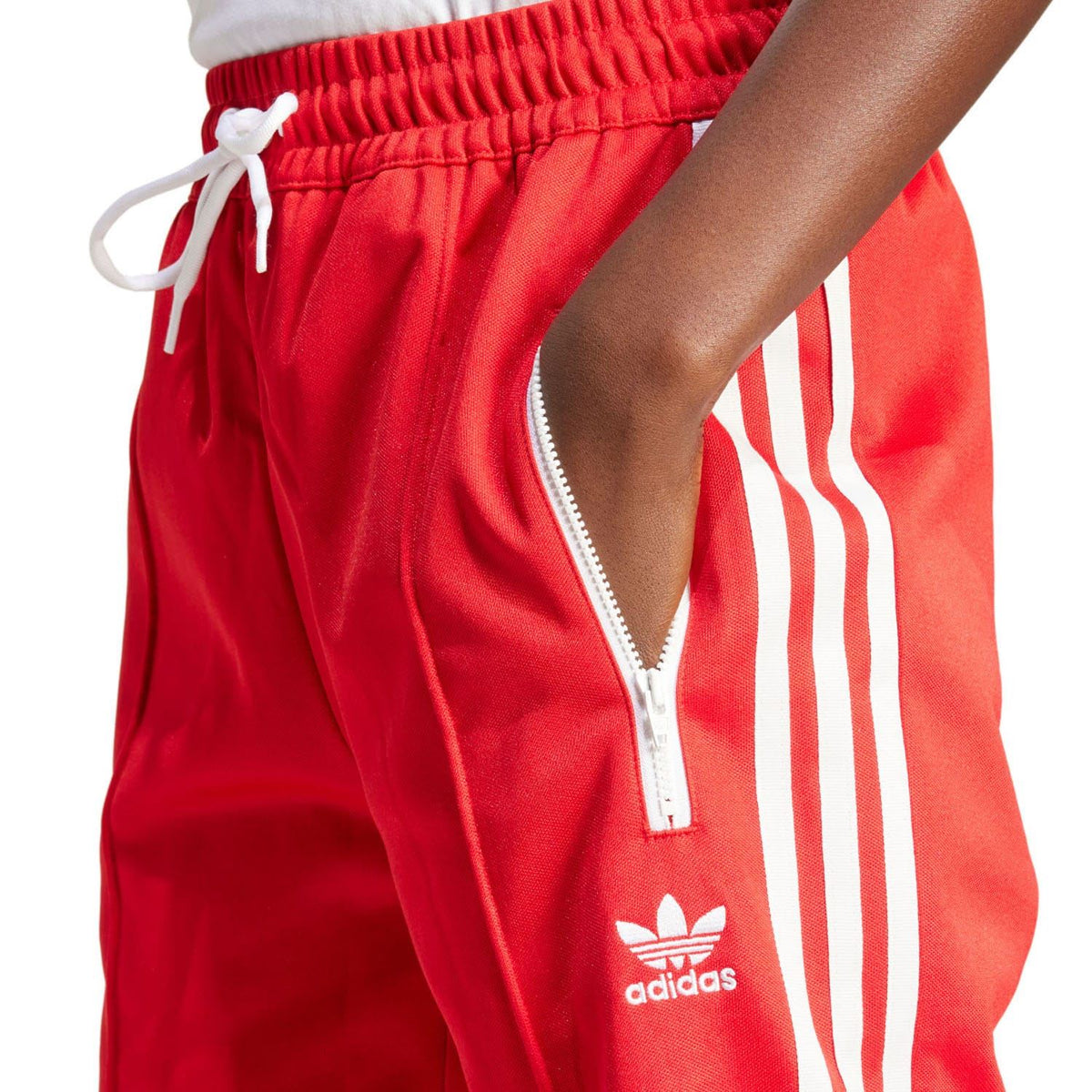 Red adidas track pants close-up: elastic waistband, drawcord tie, white logo and stripes.