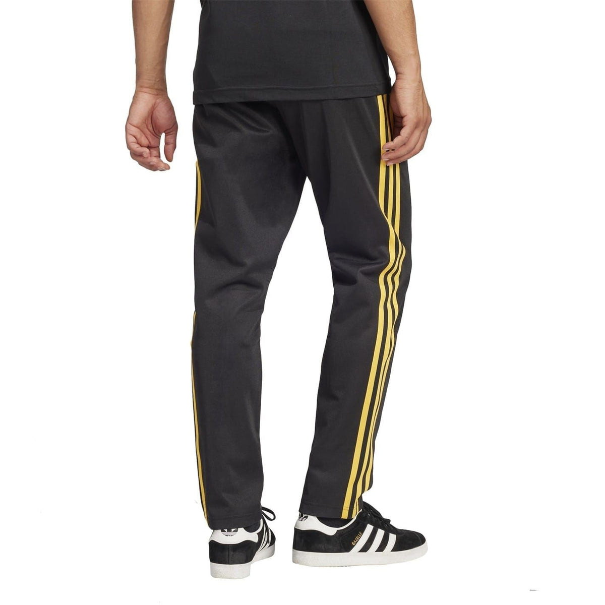 Black slim track pants with three yellow side stripes and trefoil logo, full lower-body view