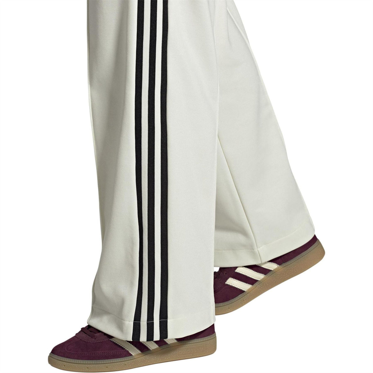 Burgundy low-top sneakers with white stripes and gum sole worn with track pants