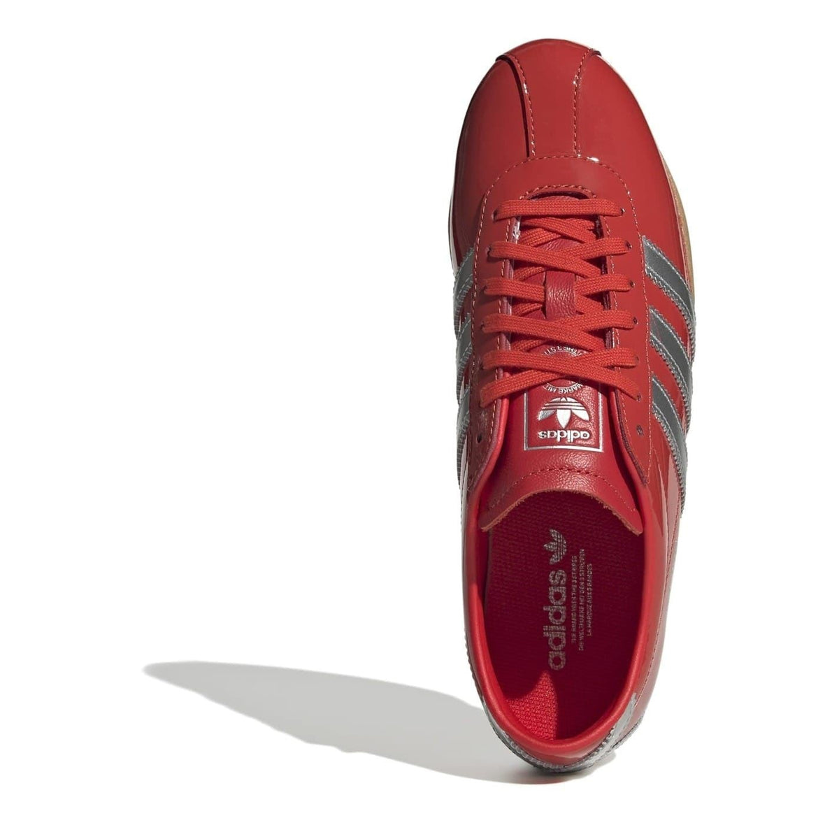 Red low-top sneaker shown from side with lace-up and metallic three-stripe detailing