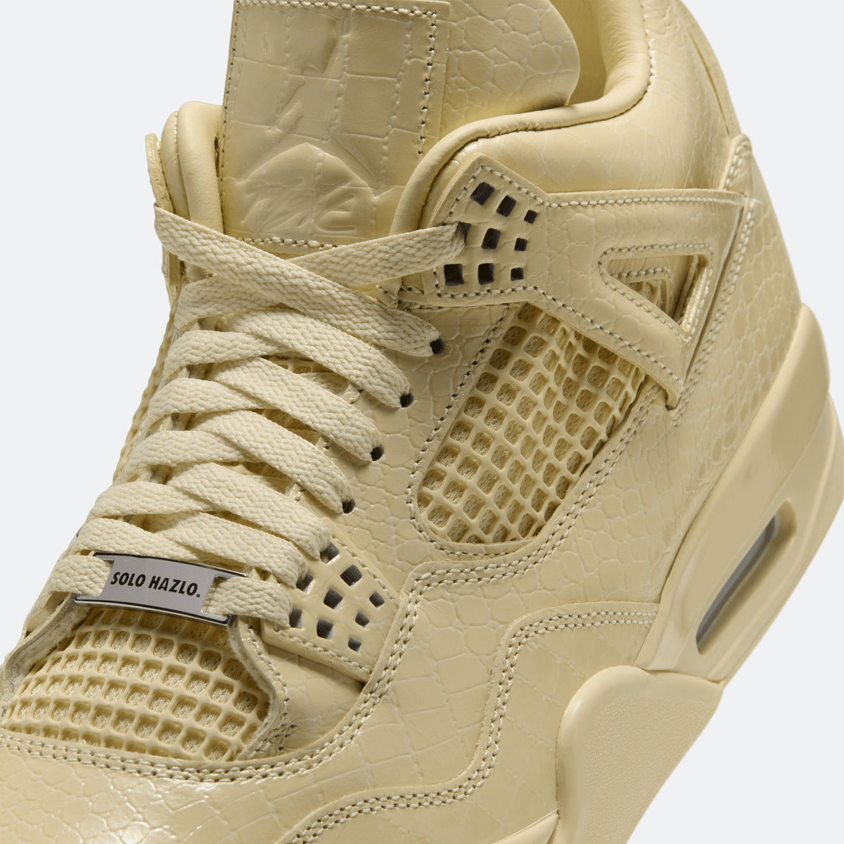 Close-up of yellow lace-up sneaker upper with textured overlays and 'SOLO HAZLO.'
