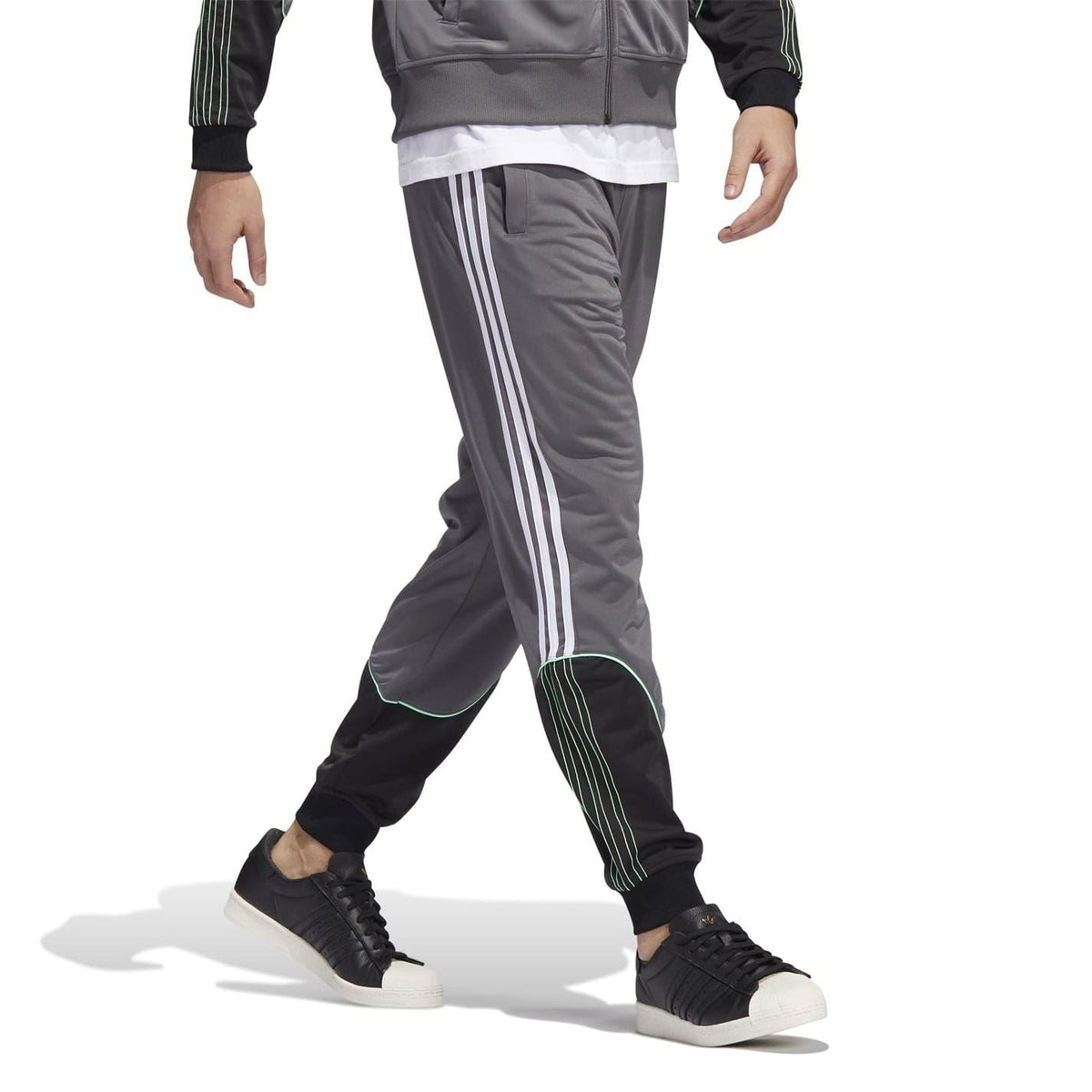Grey track sweatpants featuring three white stripes and green-trimmed pocket panels