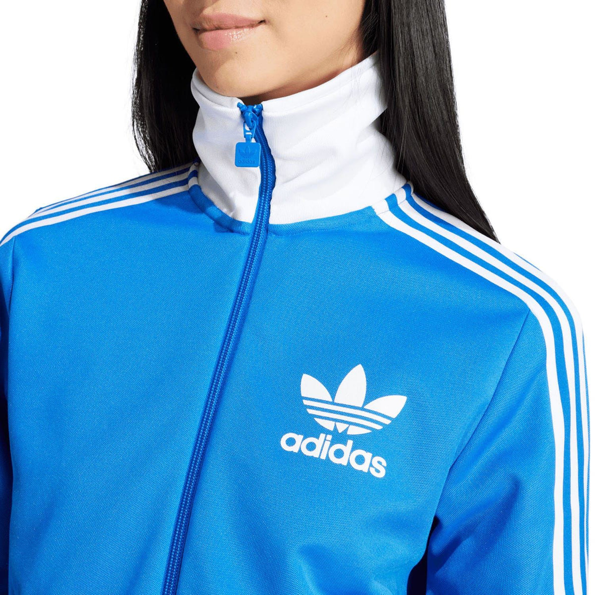 Blue track jacket close-up at chest: white adidas trefoil logo and striped shoulder detail