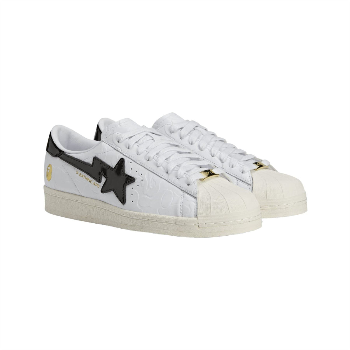 White low-top sneakers with black star emblem, gold lace hardware, and beige sole