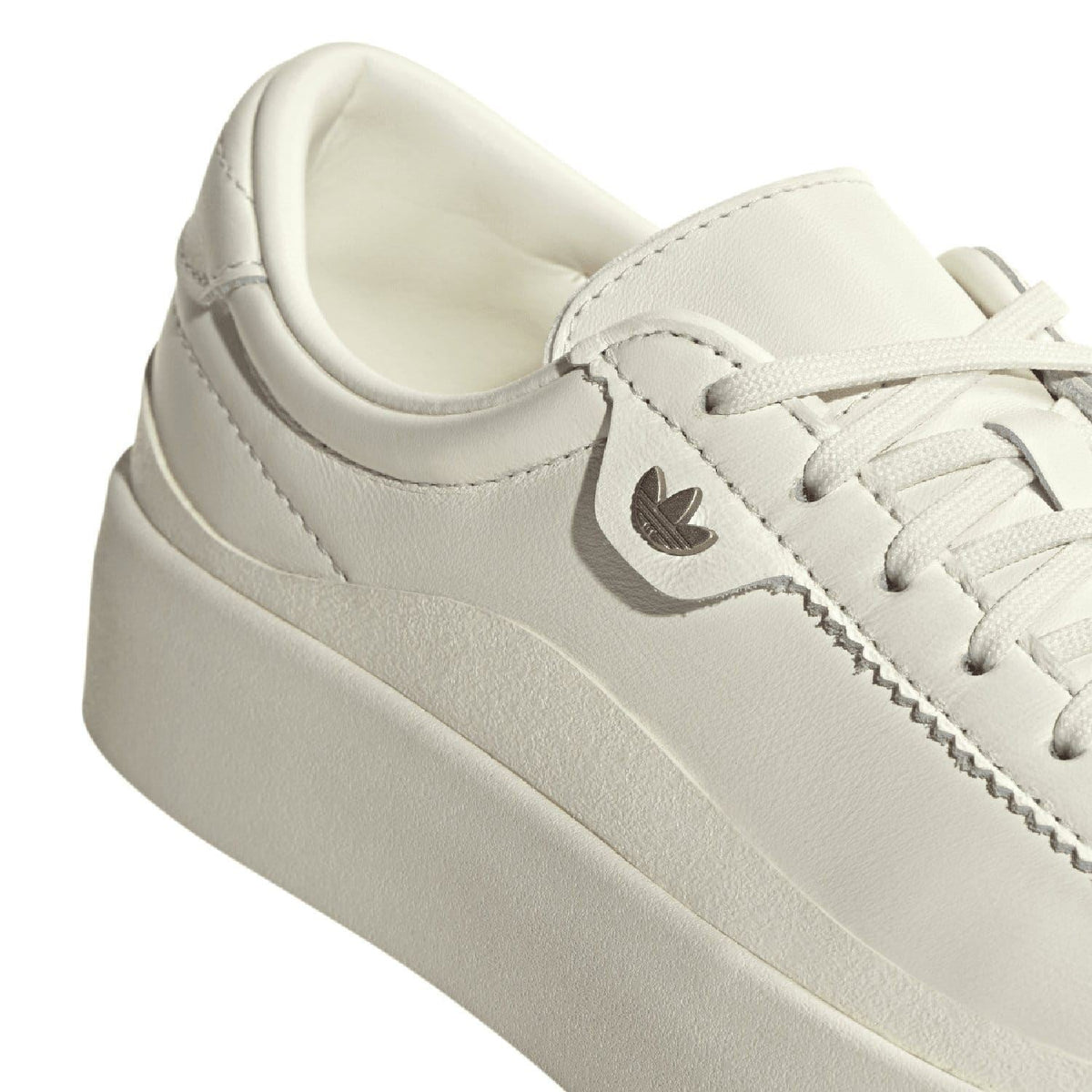White leather upper close-up with adidas Swoosh and stitched trim on chunky sole.