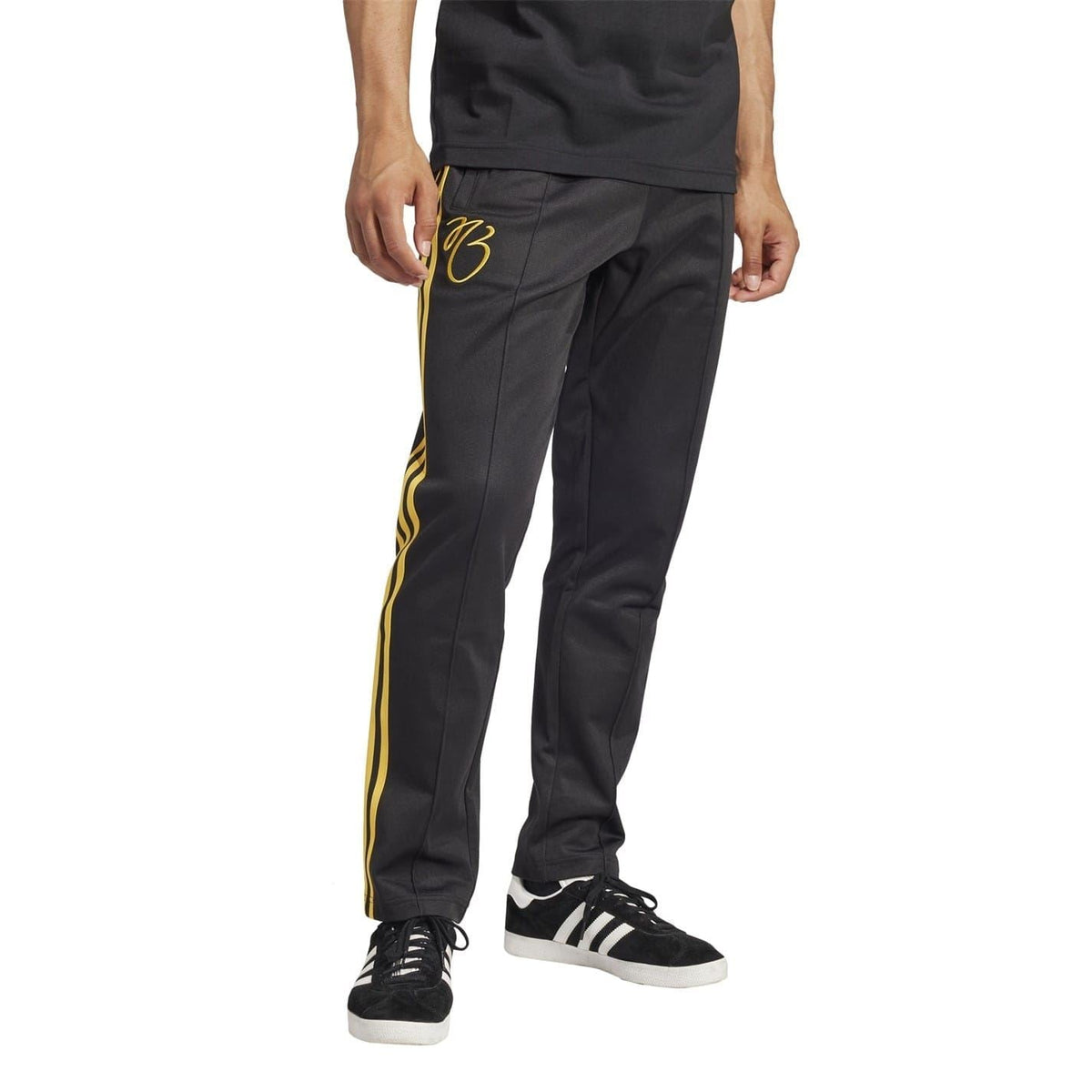 Black slim track pants with three yellow side stripes and “83” logo, shown with black sneakers