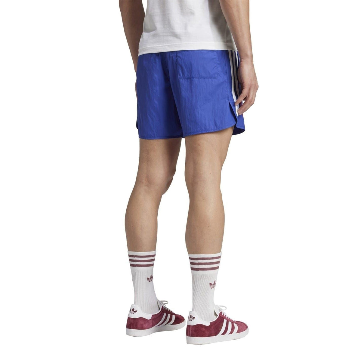 Blue soccer shorts on model with elastic waist, white side stripes, red trefoil logo