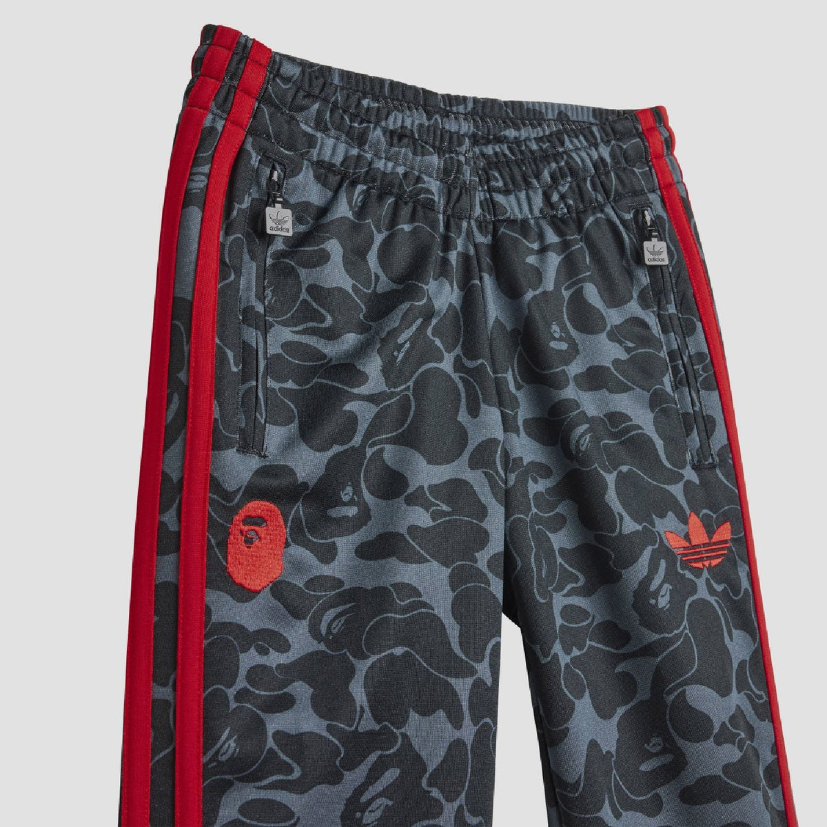 Kids camo track pants with drawstring waist, red side stripes, and red logo patch