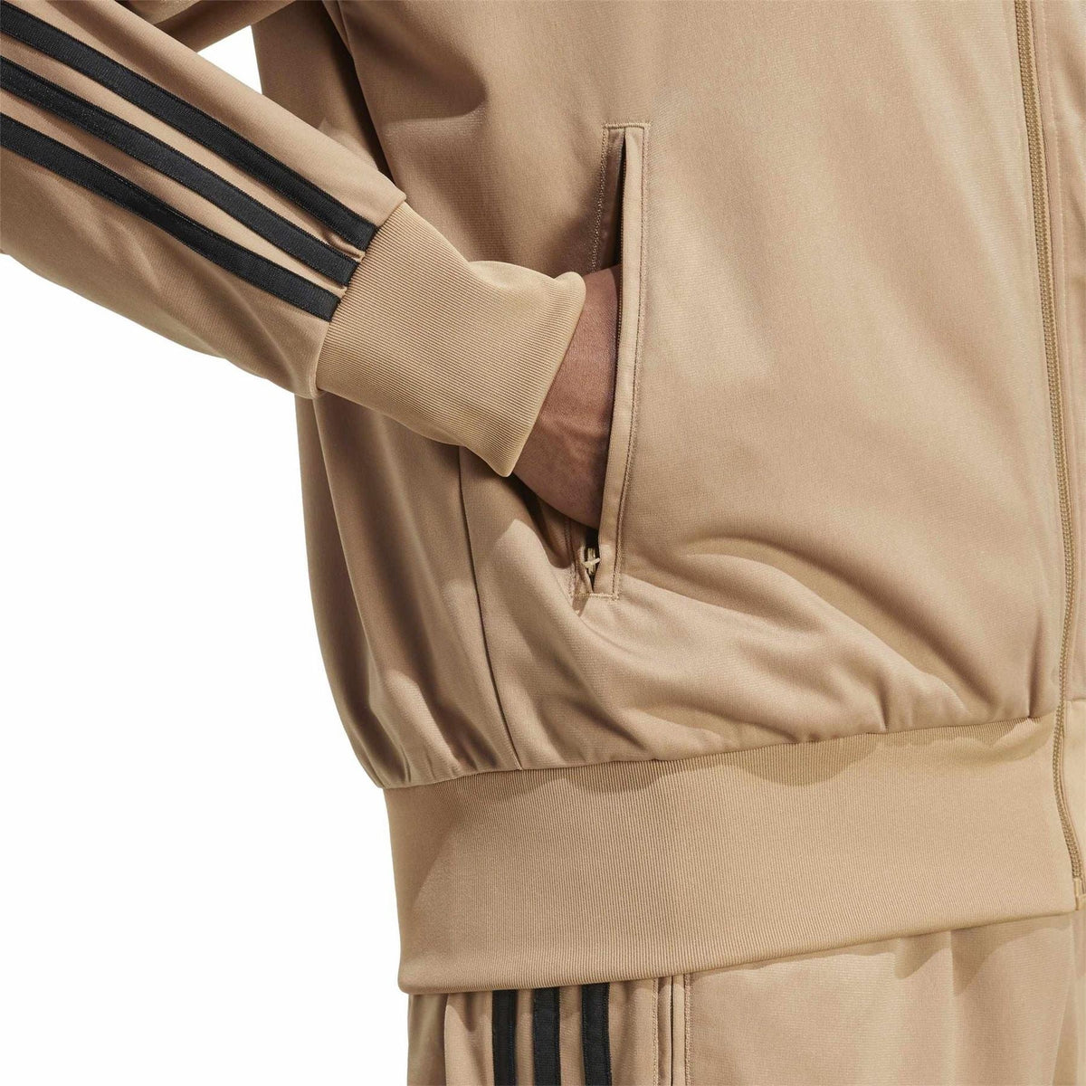 Tan track jacket close-up of zip pocket and ribbed hem with black stripe detail.