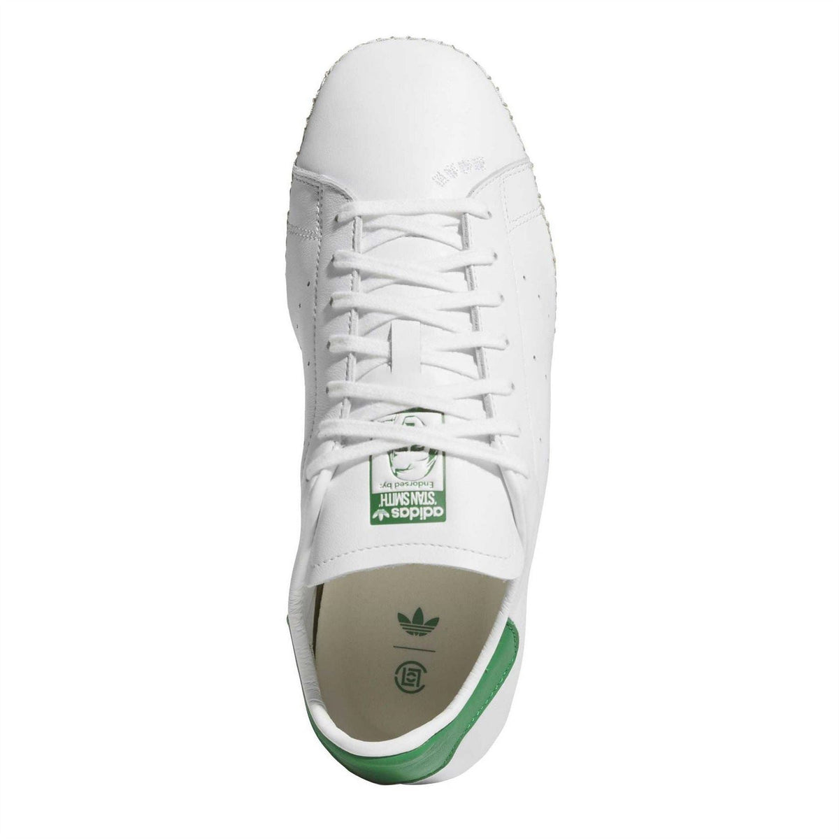 White lace-up trainers with green-and-brown logo patch on the tongue