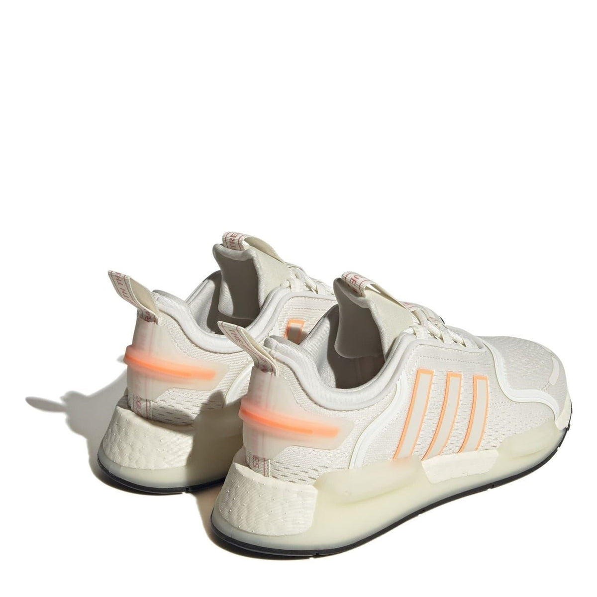 White NMD low-top sneakers with orange heel accents and black outsole, back angle