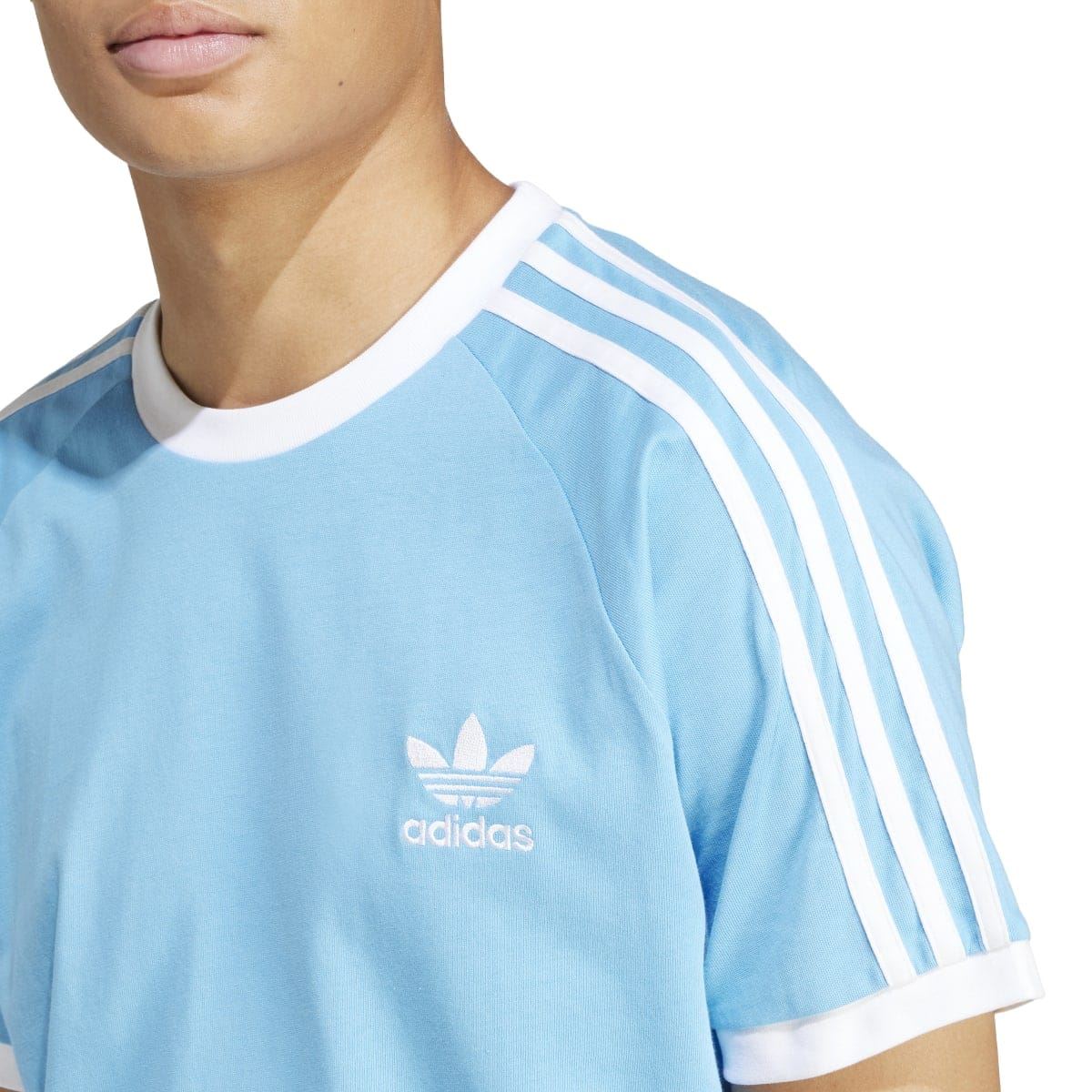 Light blue T-shirt close-up with adidas logo and white three-stripe sleeve panel