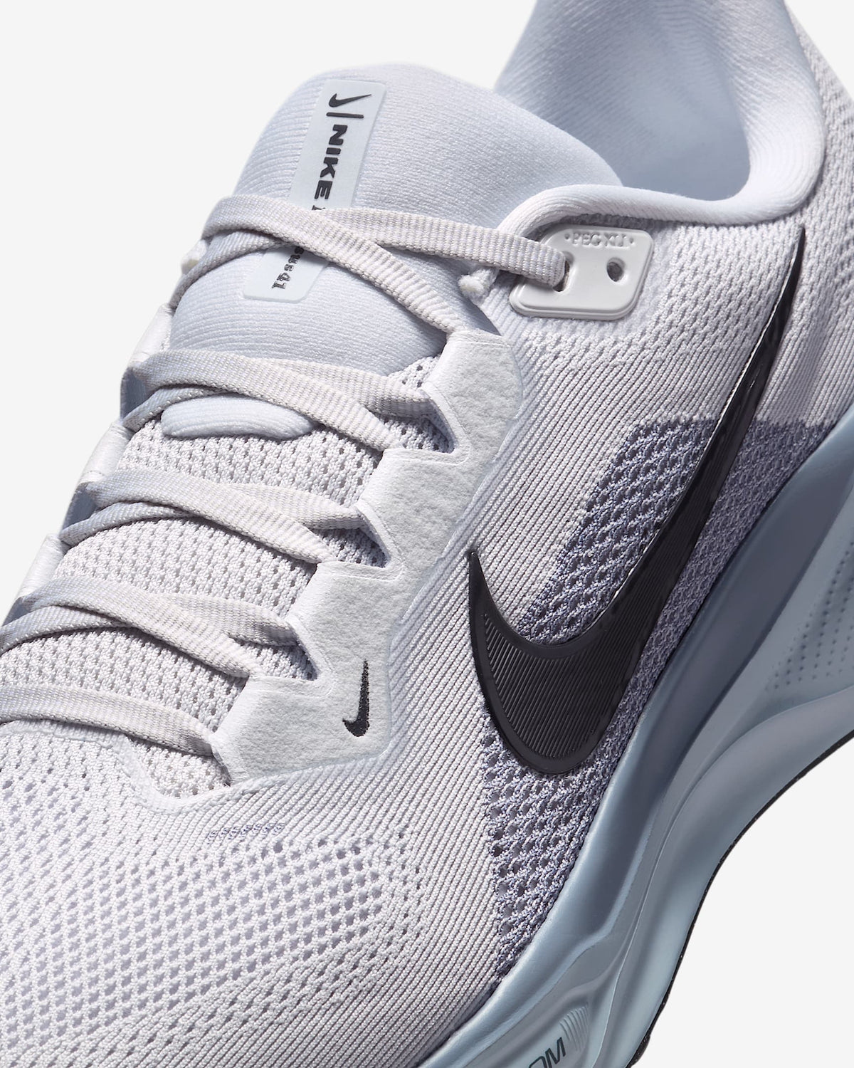 Close-up of light gray Nike running shoe upper with lace eyelets and swoosh