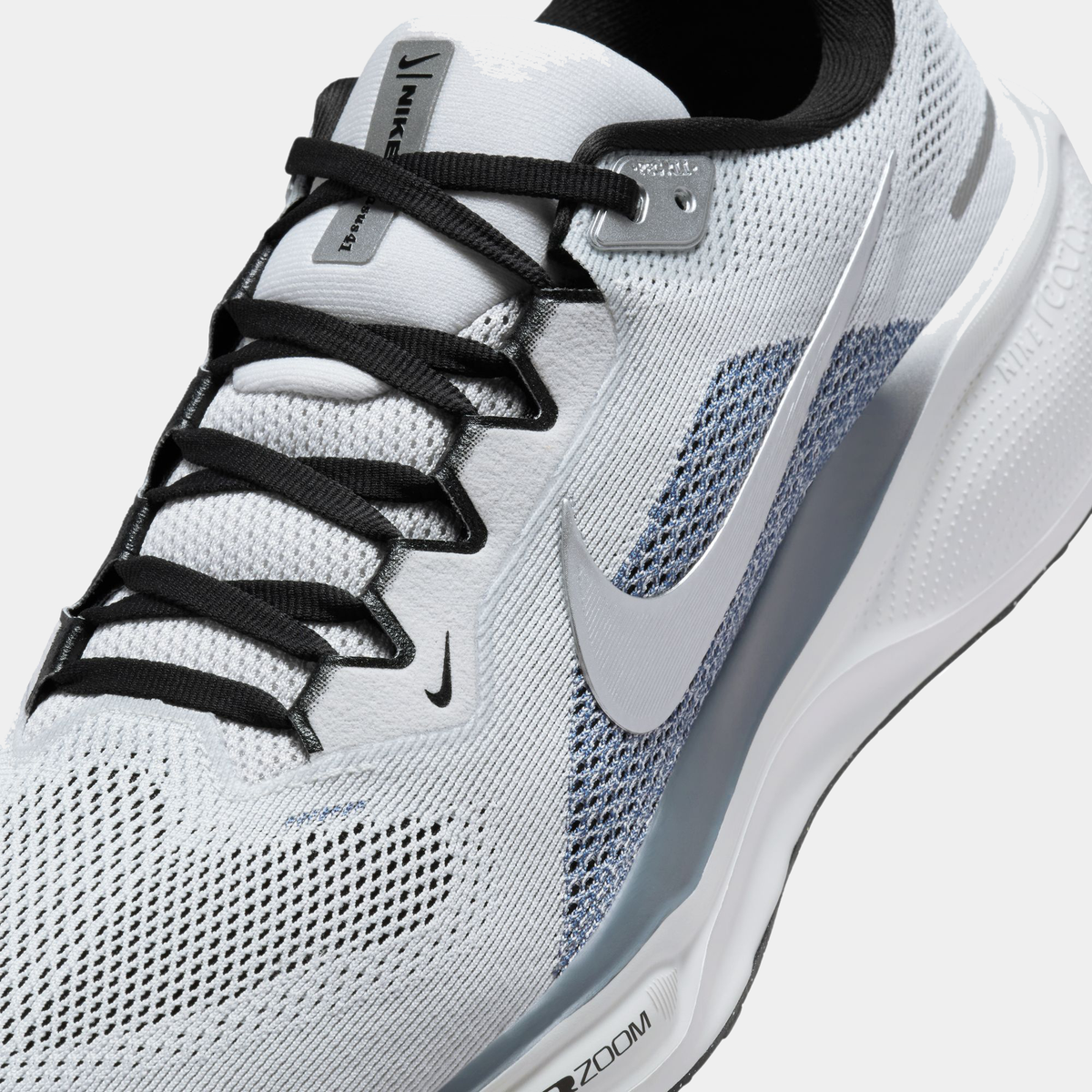 Close-up of light gray running shoe upper with navy swoosh and black lace detail