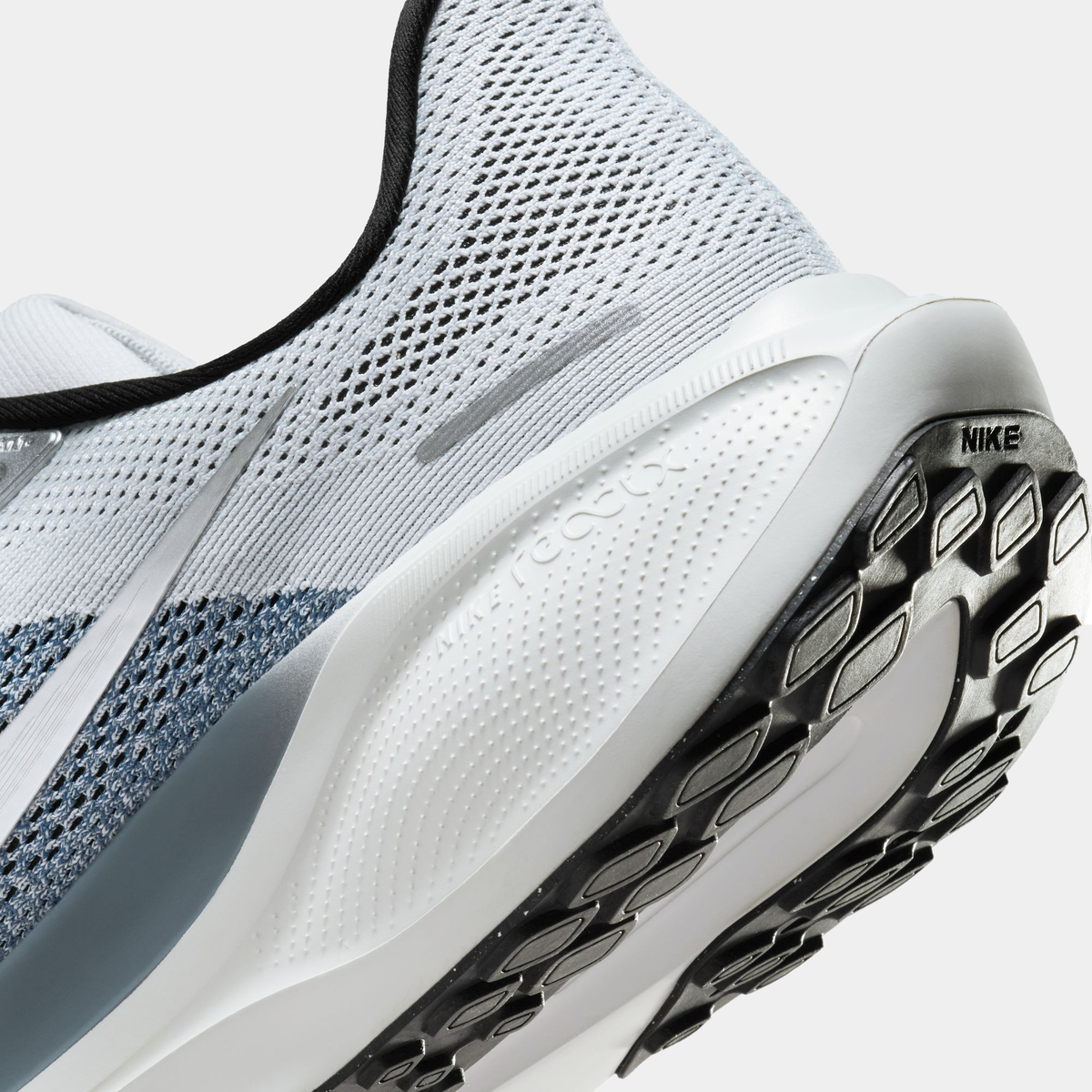 Close-up of light gray running shoe side with treaded outsole and Nike logo on heel