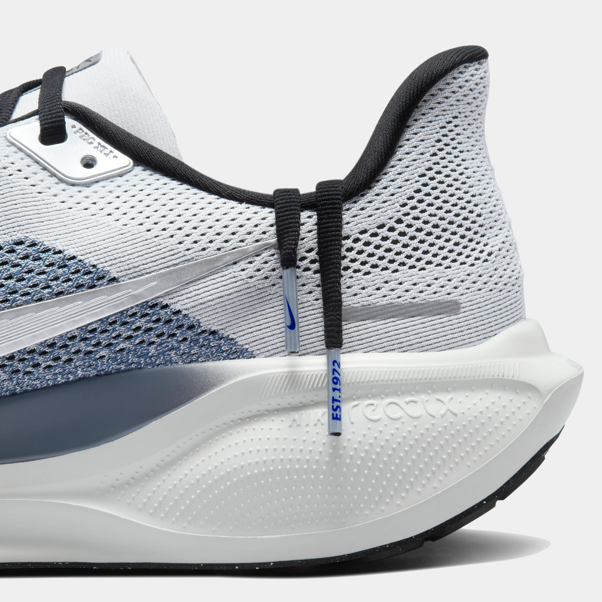 Close-up of light gray running shoe midsole with navy swoosh, black laces, blue branding
