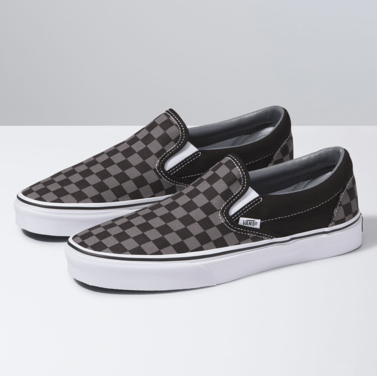 Black and gray checkerboard slip-on sneaker pair with Vans logo and white rubber sole