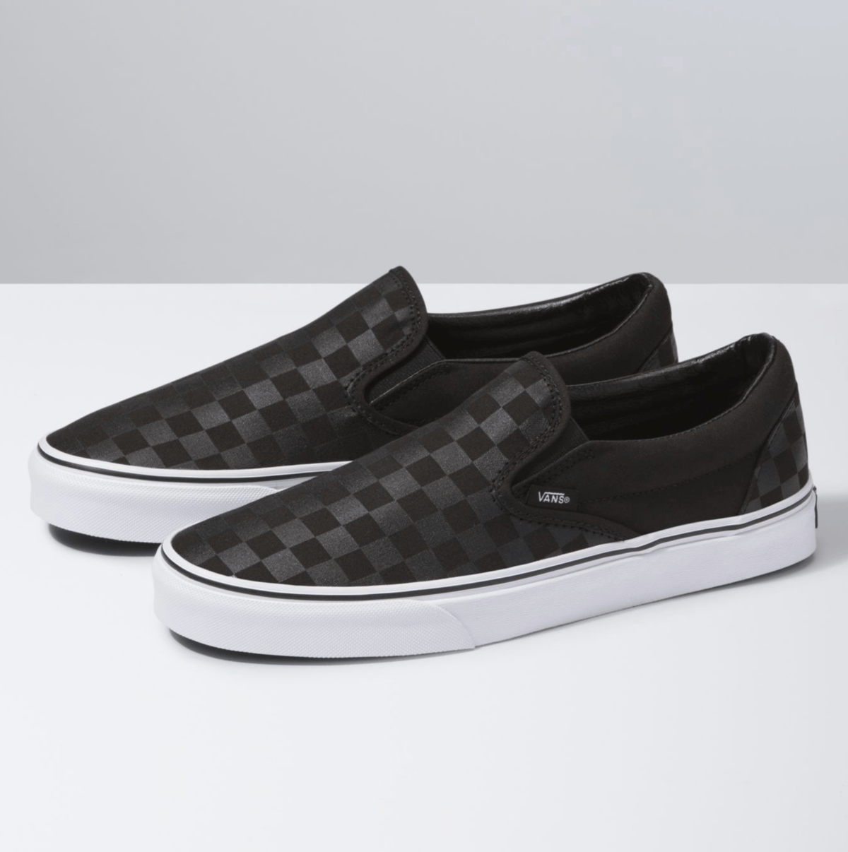Black slip-on sneakers with checkerboard pattern and white rubber sole