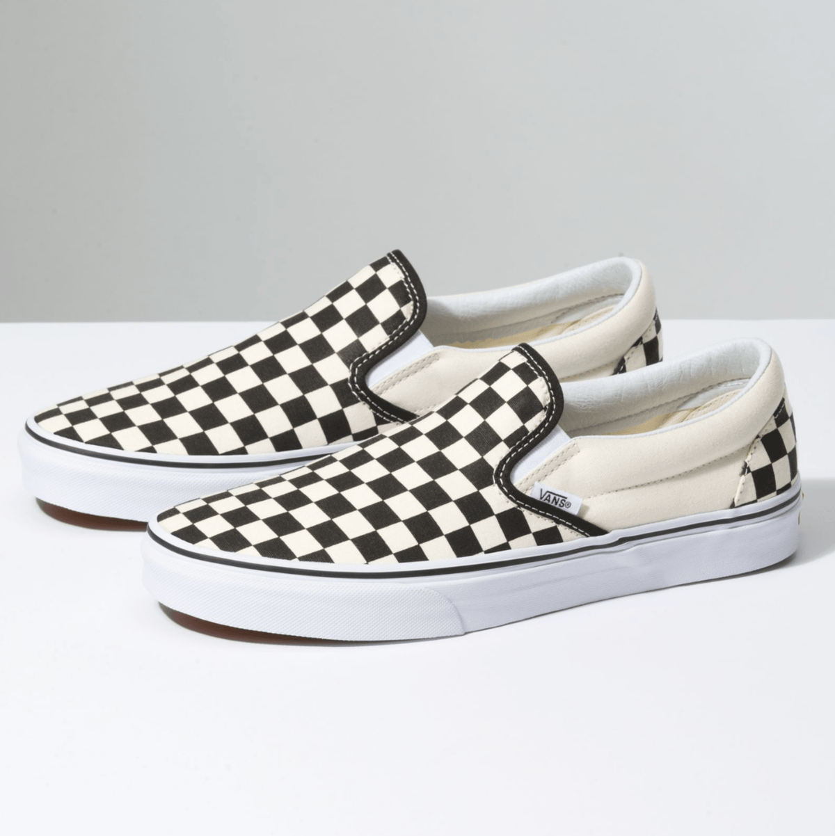 Two black-and-white checkerboard slip-on sneakers with white midsoles and trim.