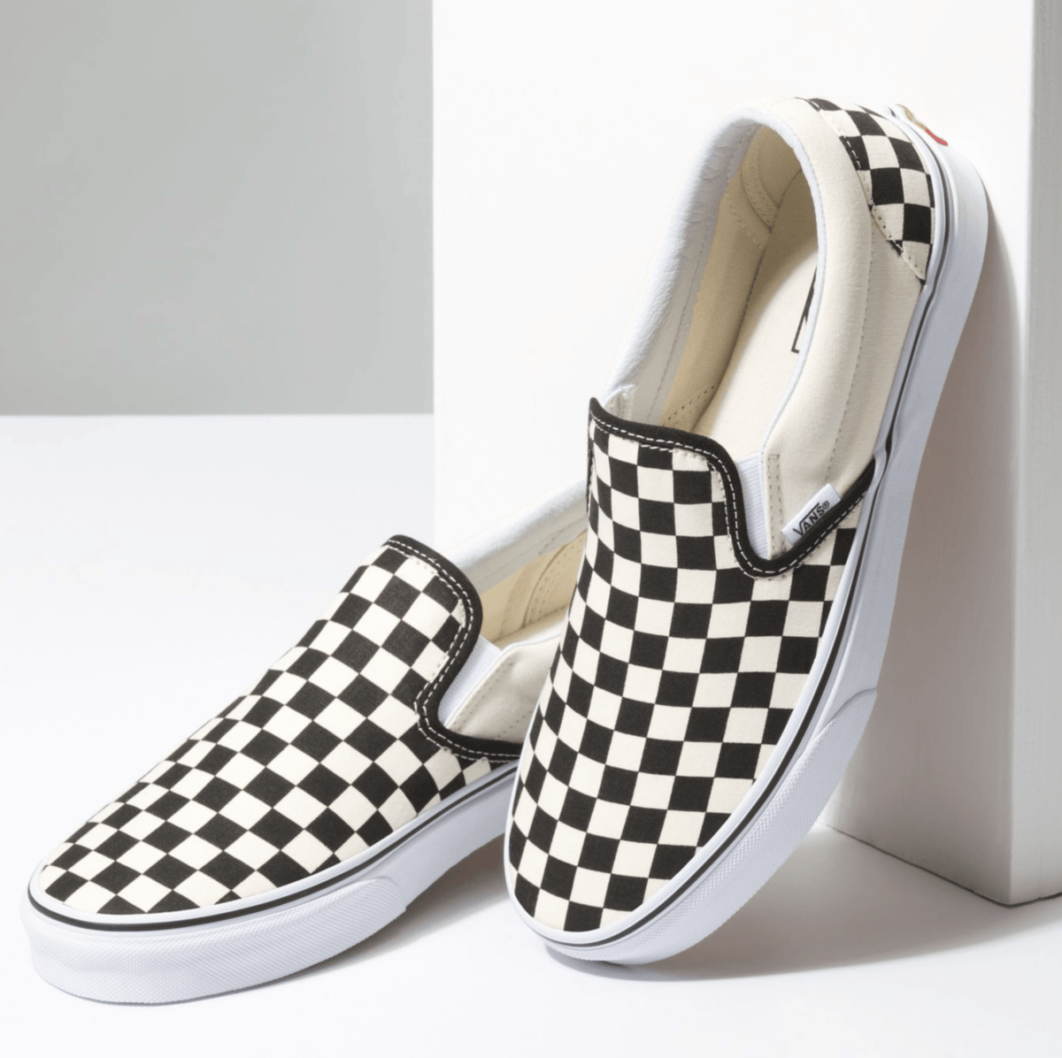 Pair of black-and-white checkerboard slip-on sneakers with white rubber midsoles.