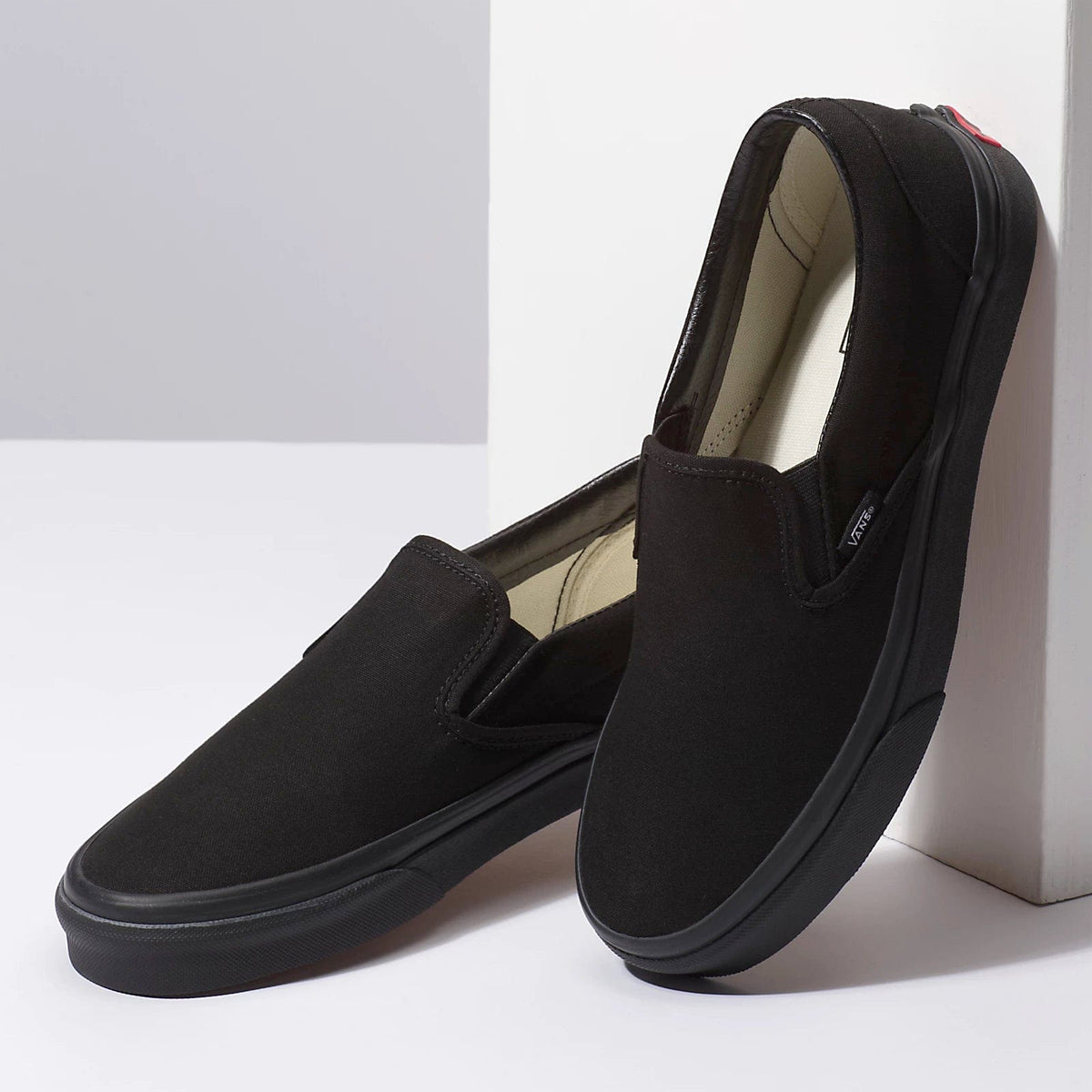 Black slip-on canvas sneakers, front and side angles, with beige interior