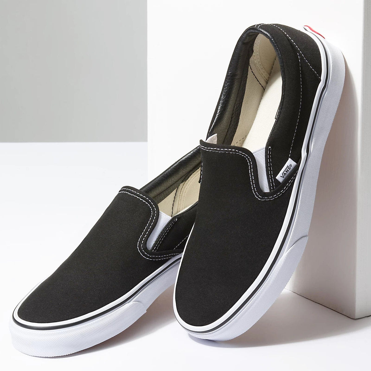 Black canvas slip-on sneaker pair with white sidewall and Vans logo patch