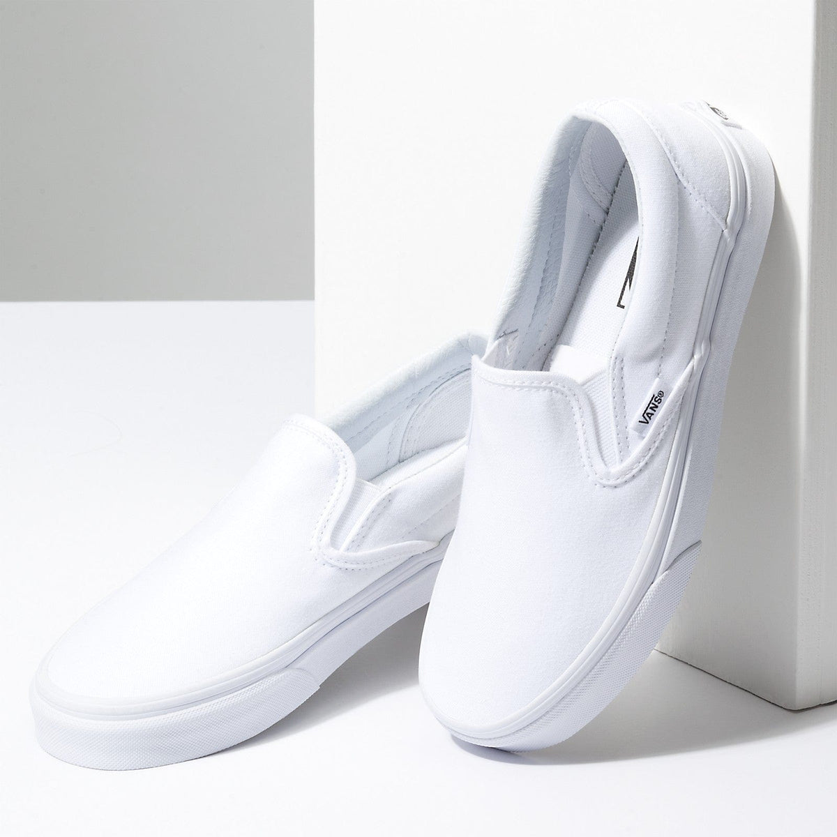 White slip-on sneakers with elastic collar and Vans logo branding on side