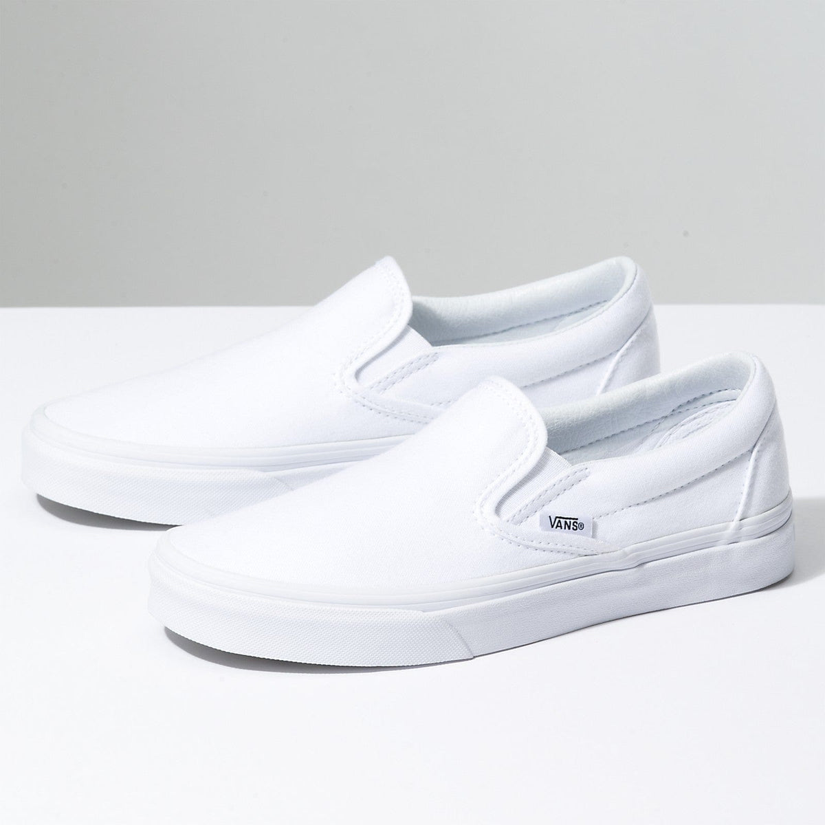 White slip-on sneakers with padded collar and Vans side logo, flat rubber sole