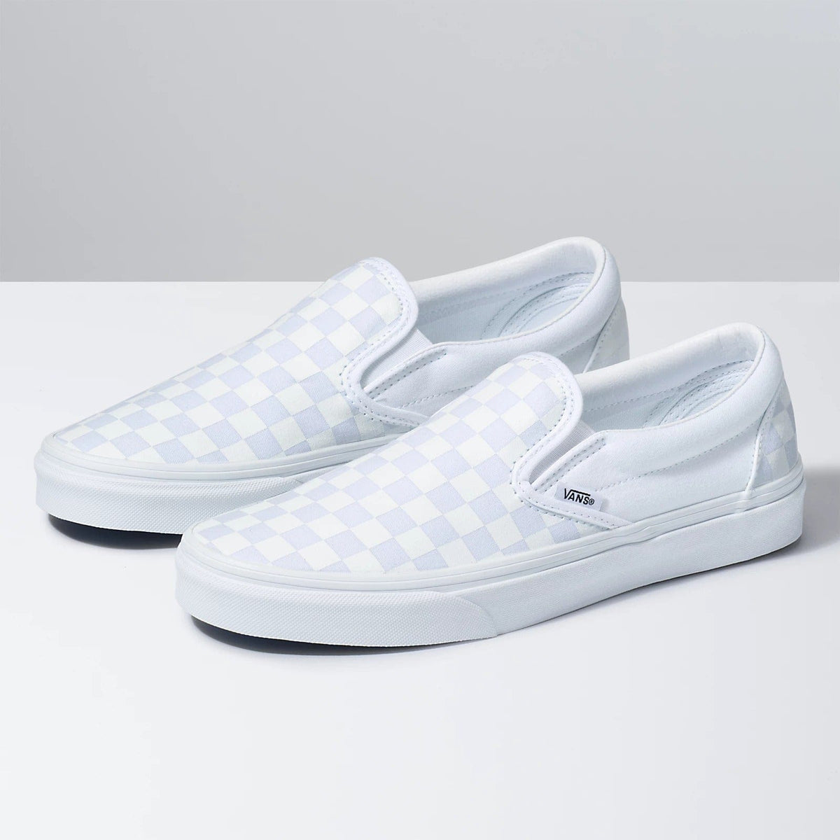 Pair of light blue checkerboard slip-on sneakers with Vans logo and white rubber sole
