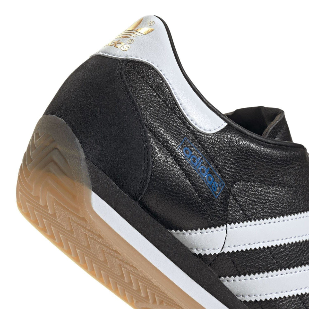 Black adidas trainers with white stripes, blue logo tab, and gum rubber outsole