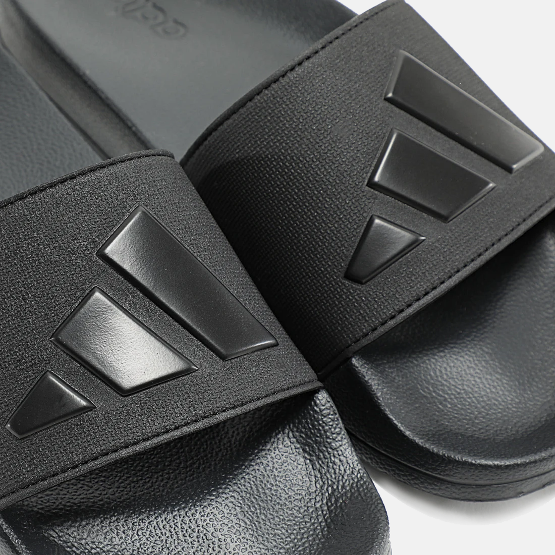 Close-up of black adidas slide sandals with embossed triple-bar logo