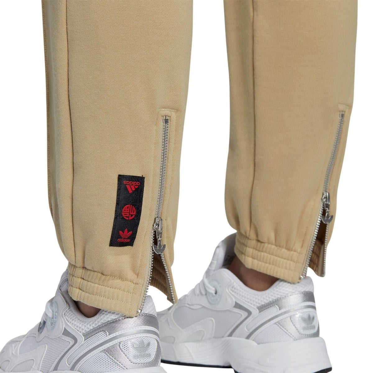 Beige sweatpants detail: front zipper pocket with logo patch near the ankle cuff