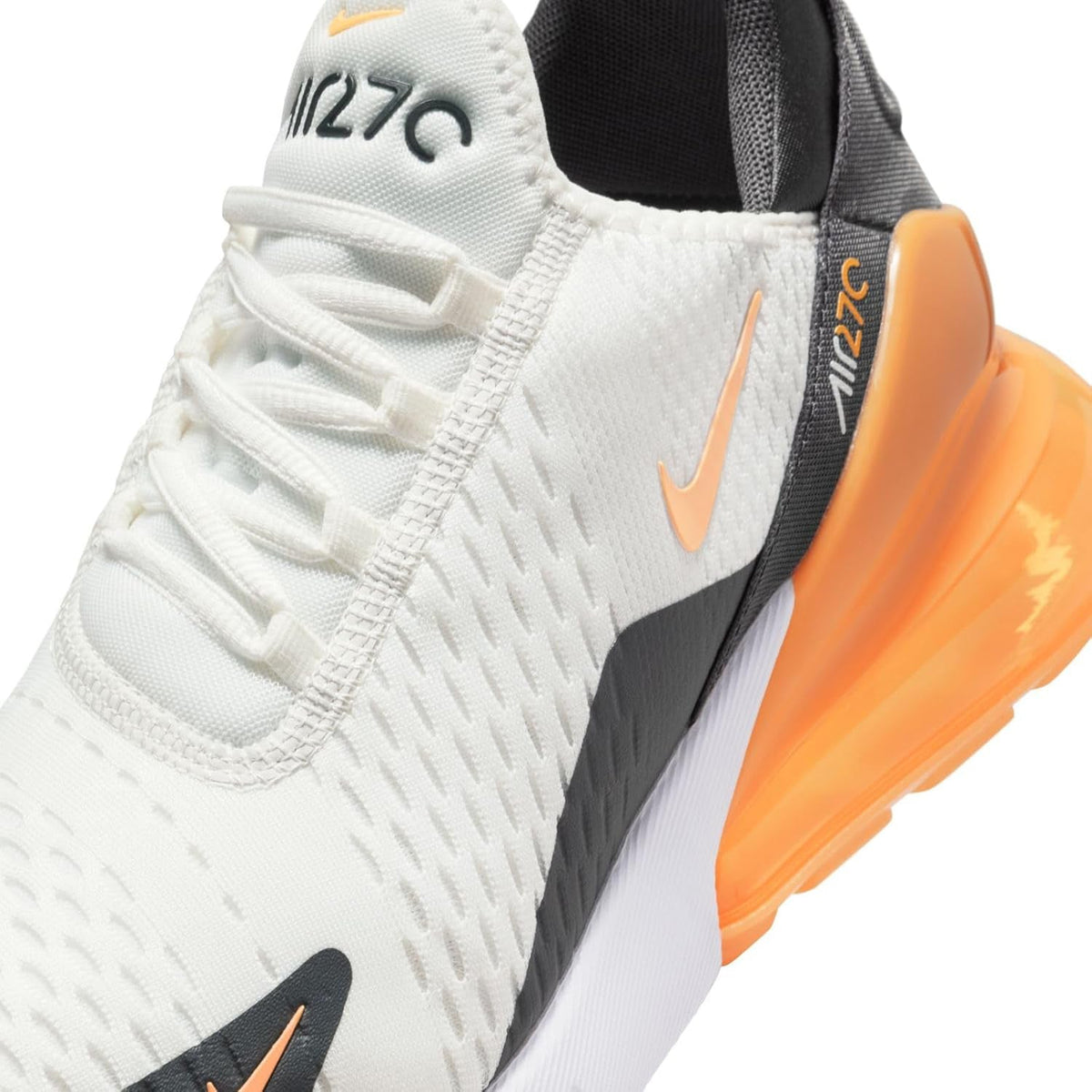 Nike Air Max 270 sneaker close-up: white knit upper, orange heel air, black strap detail.