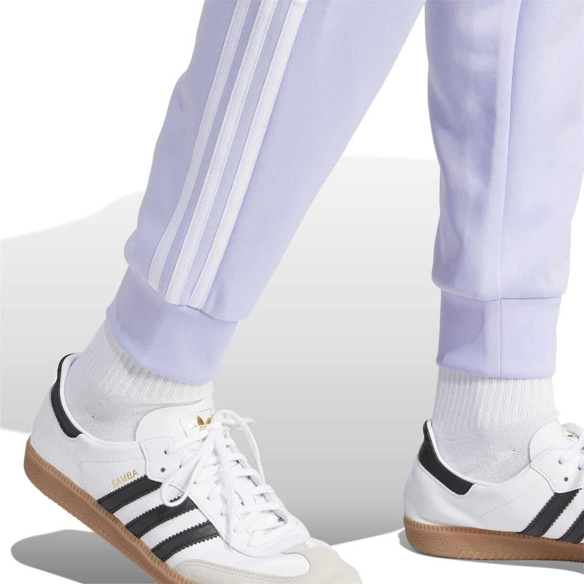 Light purple adidas track pants with three-stripe side design, shown with sneakers