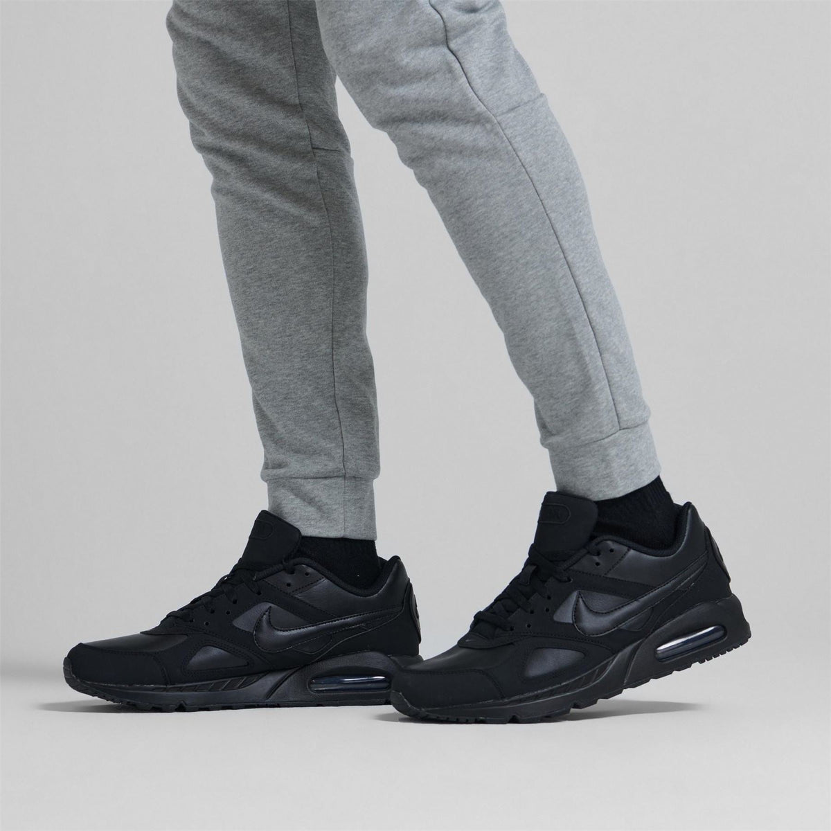 Black lace-up trainers worn with gray pants, low-profile athletic shoes