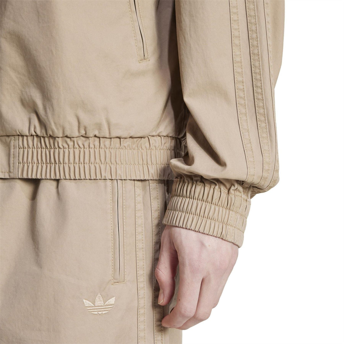 Close-up of beige jacket with elastic hem and cuffs; adidas trefoil logo