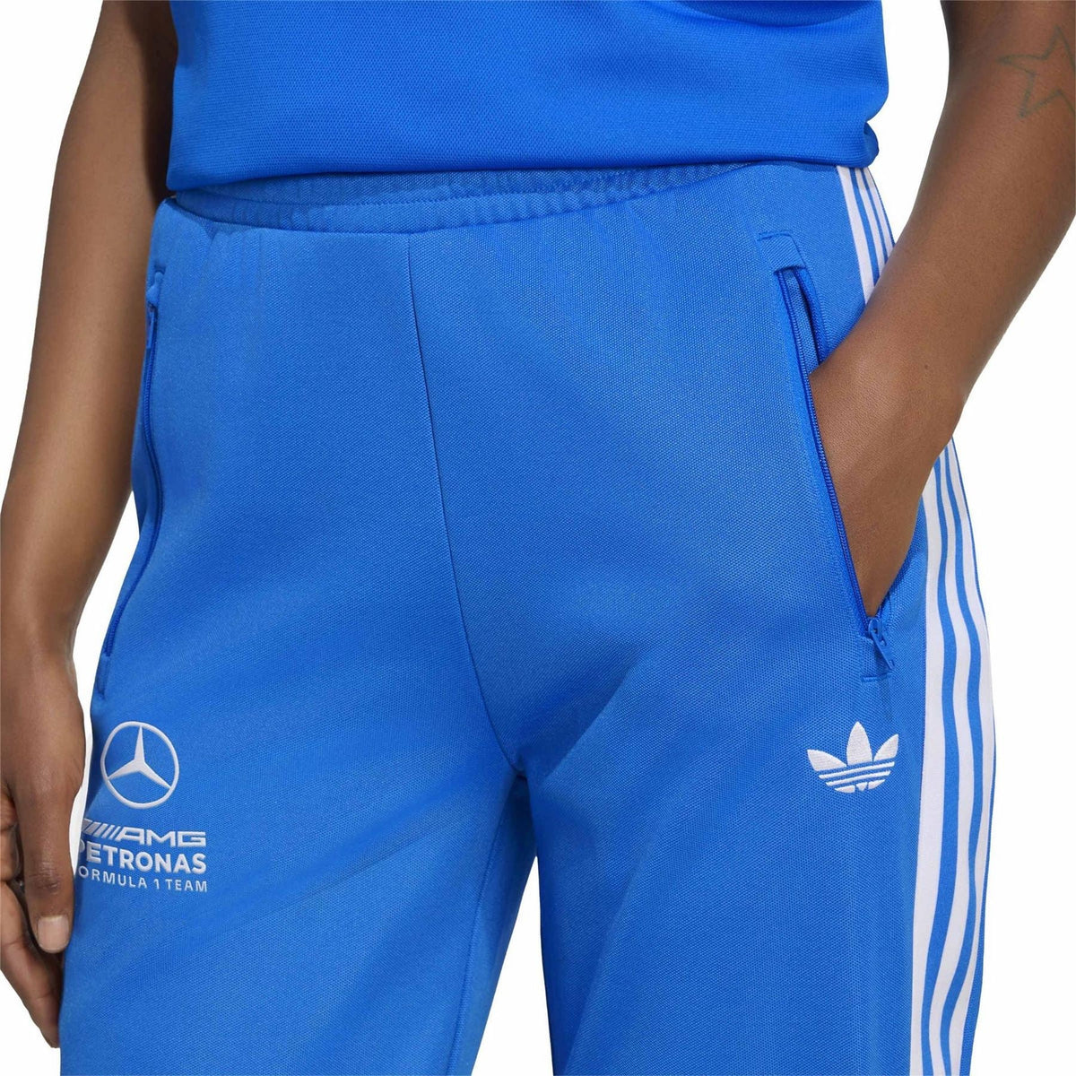 Blue track pants with white side stripes and logo prints on front leg and hem.