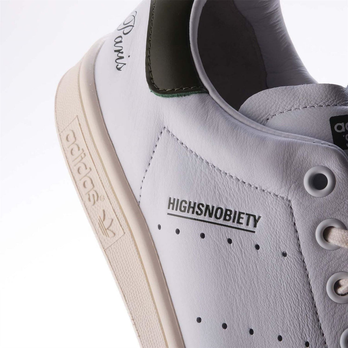 White leather sneaker side close-up with HIGHSNOBIETY lettering and perforated detail.