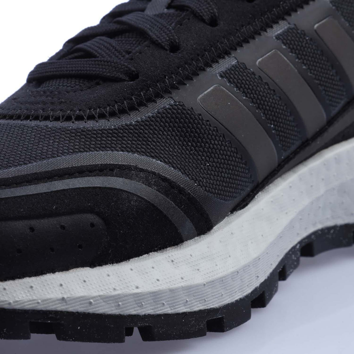 Black textured upper close-up with lace stitching and striped panel detail.