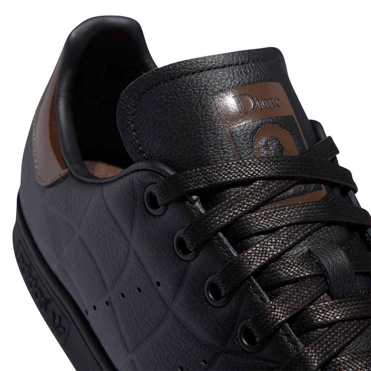 Black trainers with lace-up front and brown-and-gold Dime tongue patch
