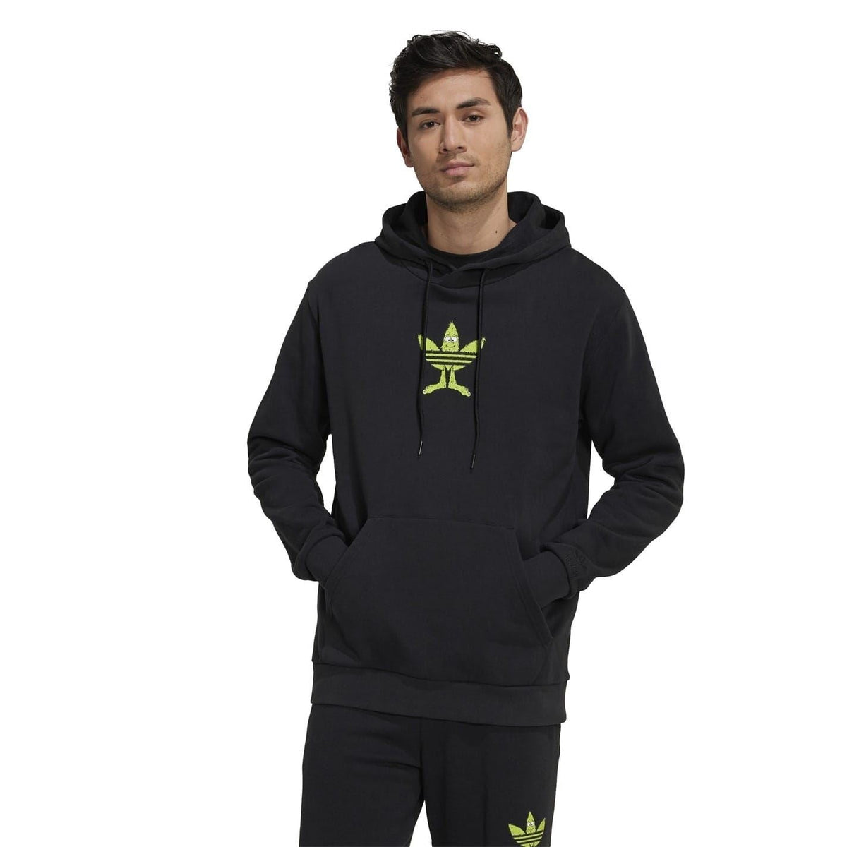 Black hooded sweatshirt on model, green trefoil logo on chest and matching logo on hem.