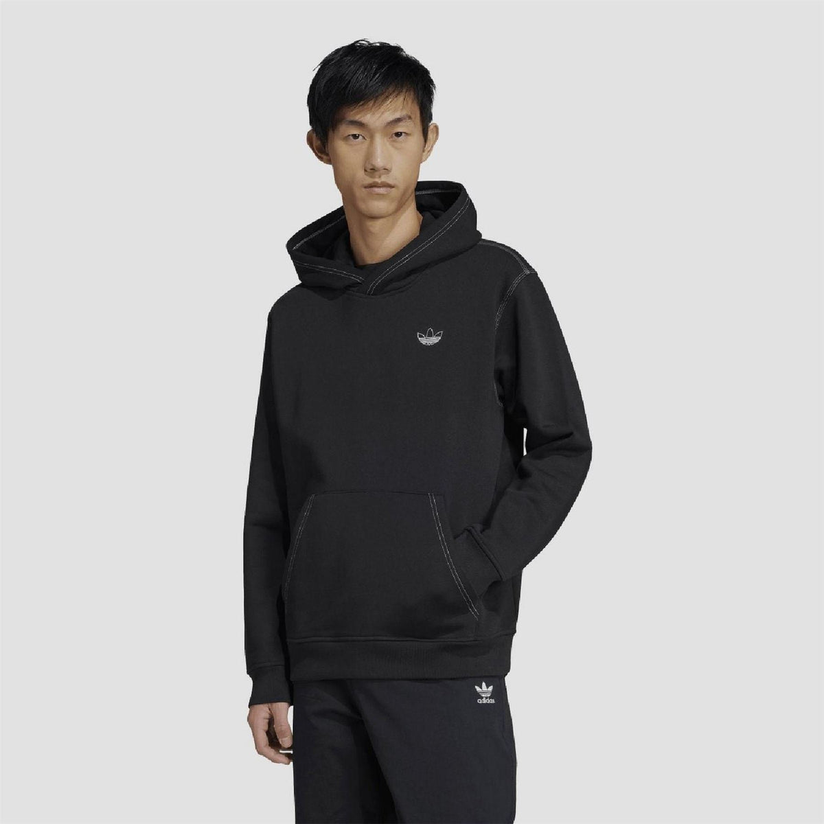 Black adidas Originals hoodie on model, featuring pouch pocket and small chest logo