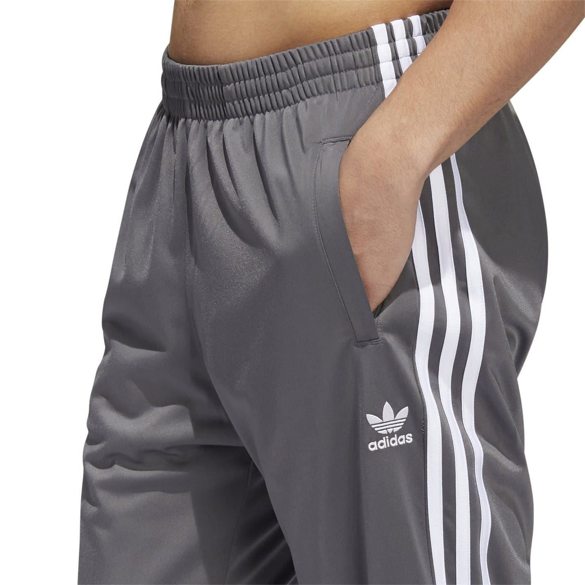 Grey track sweatpants close-up with elastic waistband, adidas logo, and side stripes