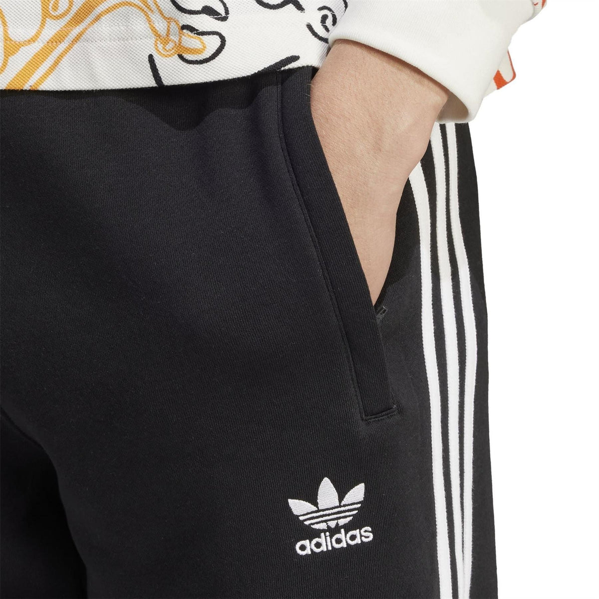 Black slim joggers with white side stripes and adidas trefoil logo at hip