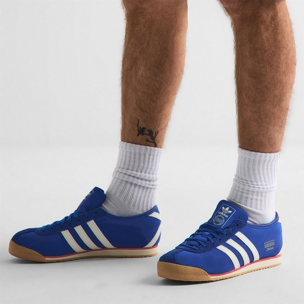Royal blue low-top trainers on feet with white stripes and gum sole
