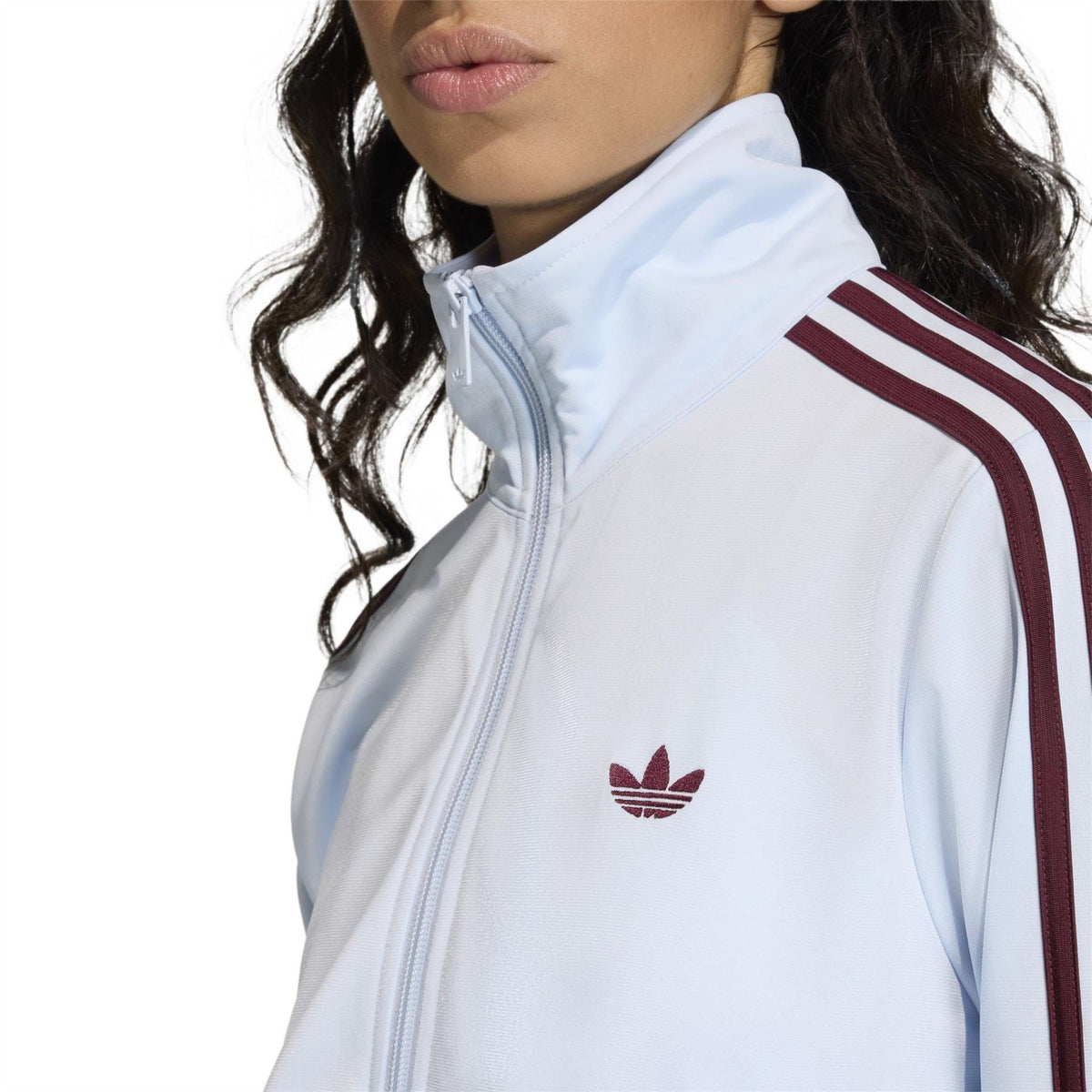 Light blue women’s track jacket close-up: standing collar, zip front, burgundy stripes, logo.